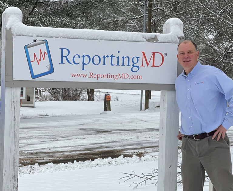 a man standing next to a ReportingMD sign